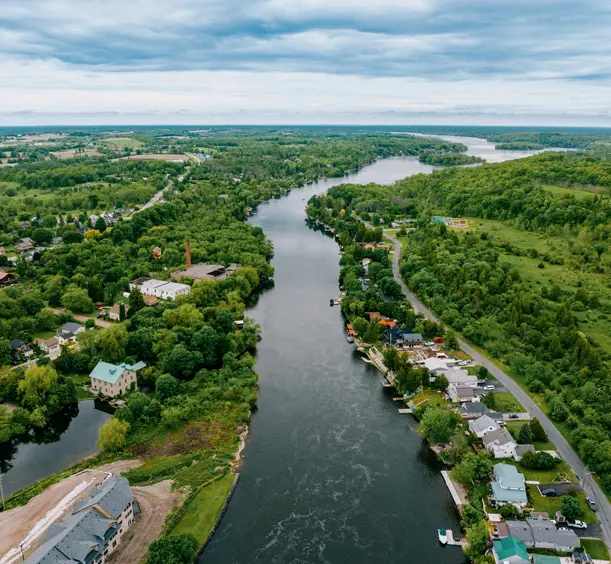 Aerial view of Hastings, Ontario, showing a winding river lined with homes and trees, stretching through a lush, green rural landscape.