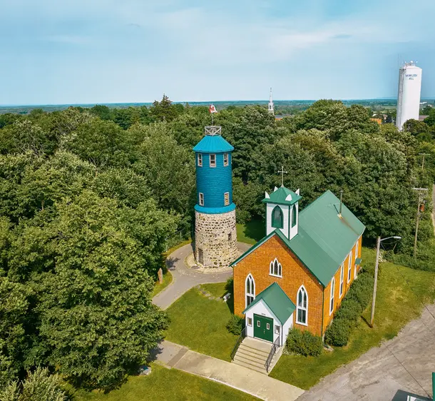 Luftaufnahme des Higginson Towers und der St. John the Apostle Anglikanischen Kirche in Vankleek Hill, umgeben von grünen Bäumen an einem Sommertag.