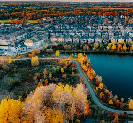 Vue aérienne d’une banlieue de Woodbridge avec des rangées de maisons, un petit lac, des sentiers sinueux et des arbres d’automne colorés.