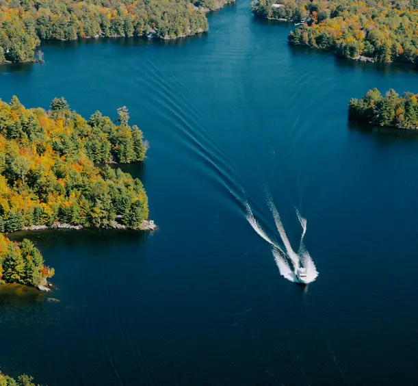 Two boats cruising on a blue lake leaving white trails, surrounded by forested shoreline in Orillia and Lake Country.