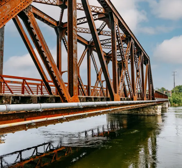Eisenbahnbrücke in rostfarben über den Otonabee River entlang des Trans Canada Trail in Peterborough, im ruhigen Wasser gespiegelt.
