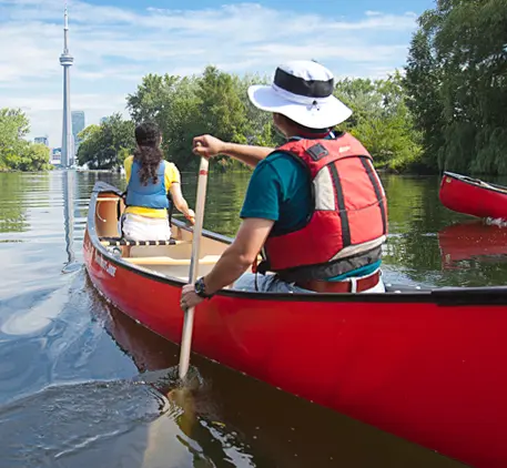 Un homme et une femme en canot sur des eaux calmes, avec la Tour CN en arrière-plan.