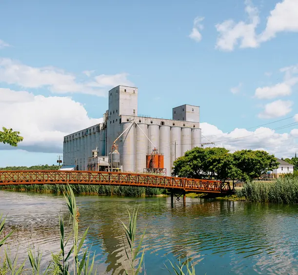 The Owen Sound grain elevators and metal bridge reflected in the harbour on a sunny summer day with scattered clouds.