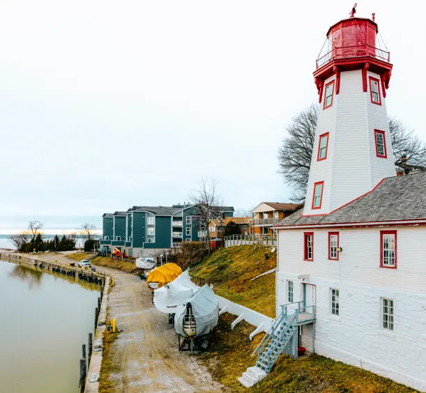 White and red octagonal Kincardine Lighthouse by the Lake Huron shoreline on a cloudy day, with boats stored nearby.