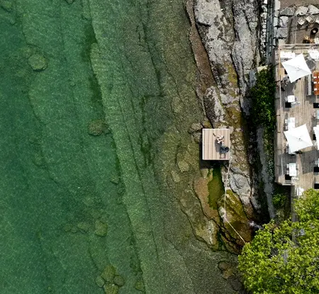 바위 해안과 푸른색 온타리오 호수를 바라보는 레이크사이드 모텔의 햇볕이 잘 드는 데크를 공중에서 본 모습입니다.