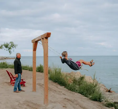 Un homme se tenant debout à côté d’une femme se balançant sur une balançoire sur les bancs de sable du lac Érié.
