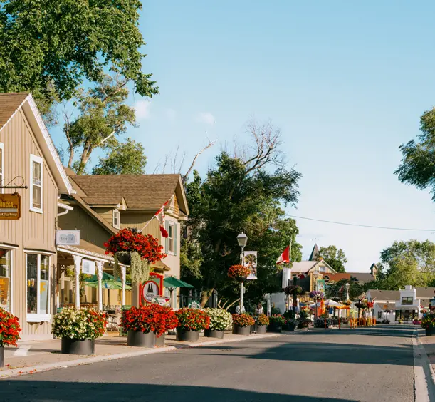 Une rue principale fleurie à Unionville, en Ontario, bordée de bâtiments patrimoniaux, de terrasses et de boutiques par une journée ensoleillée.
