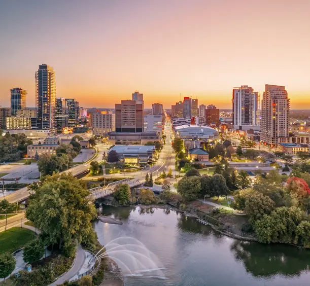 City skyline of London, Ontario at sunset, with the river winding through the scene beneath a colourful sky.