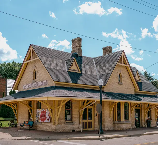 Station Arts Centre in Tillsonburg, housed in a restored historic railway station, pictured on a sunny summer day with scattered clouds.