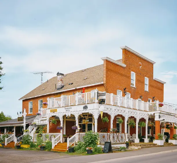 Die rote Backsteinfassade des Tamworth Hotels mit bezaubernden weißen Rundumbalkonen und Hängepflanzen an einem bewölkten Sommertag.