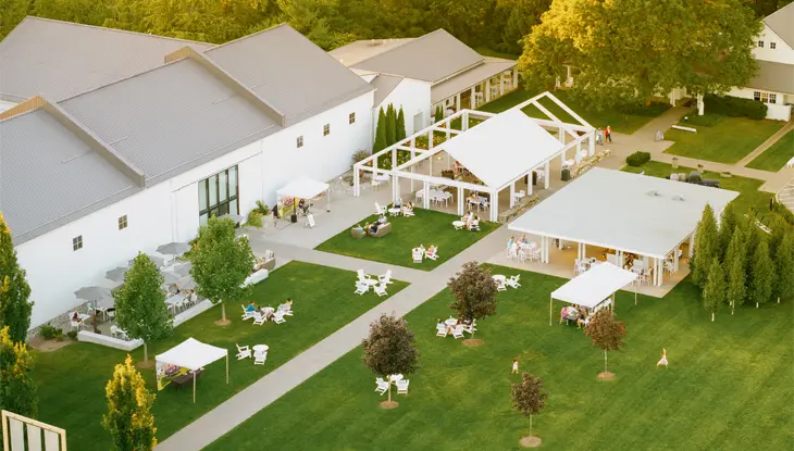 Outdoor event space at 13th Street Winery in St. Catharines, featuring white buildings, tents and seating areas surrounded by lush greenery.