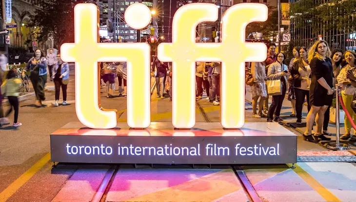 A large neon TIFF sign stands outside a theatre with crowds of moviegoers during the Toronto International Film Festival.