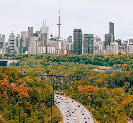 Vue du paysage urbain d'une autoroute menant vers l'horizon de Toronto entourée d'une forêt avec un feuillage d'automne.