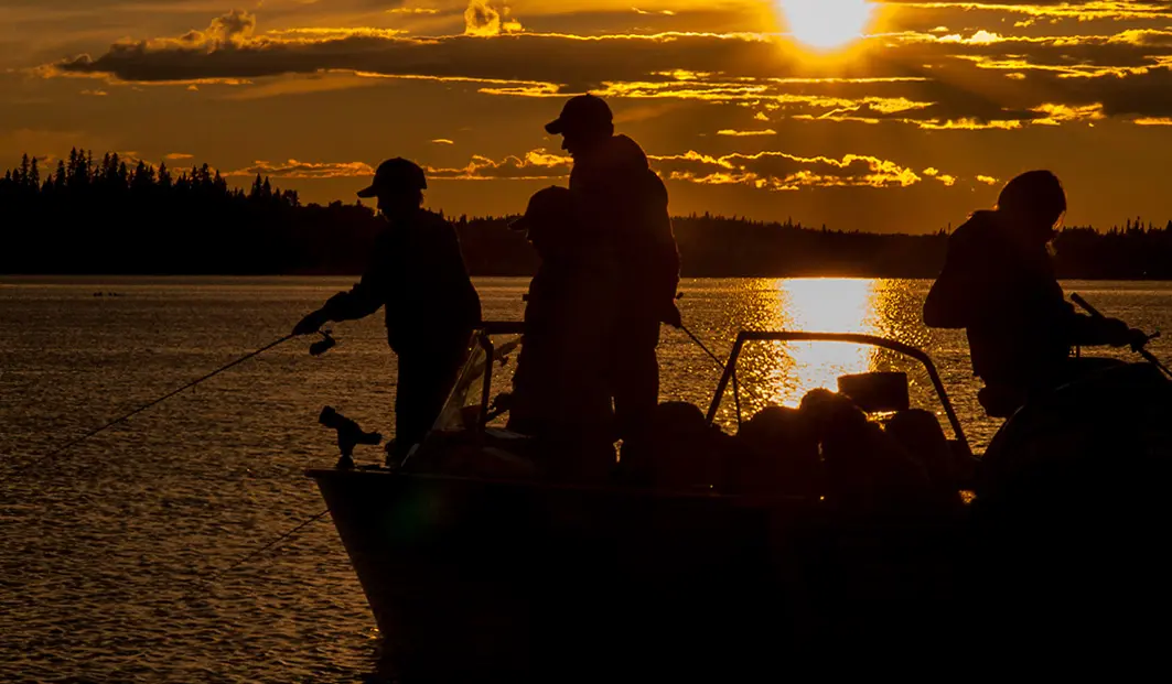 Drei Personen angeln bei Sonnenuntergang von einem Boot im Fushimi Provincial Park. 