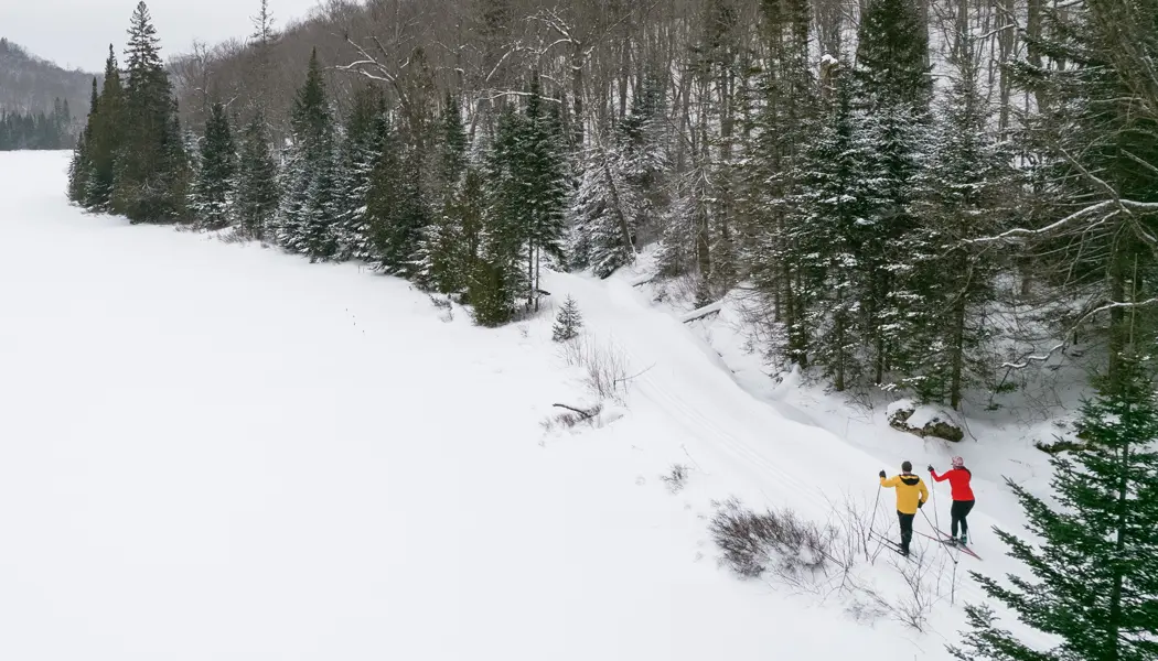 A couple cross-country skiing on a snowy trail alongside a forest at Stokely Creek Lodge.