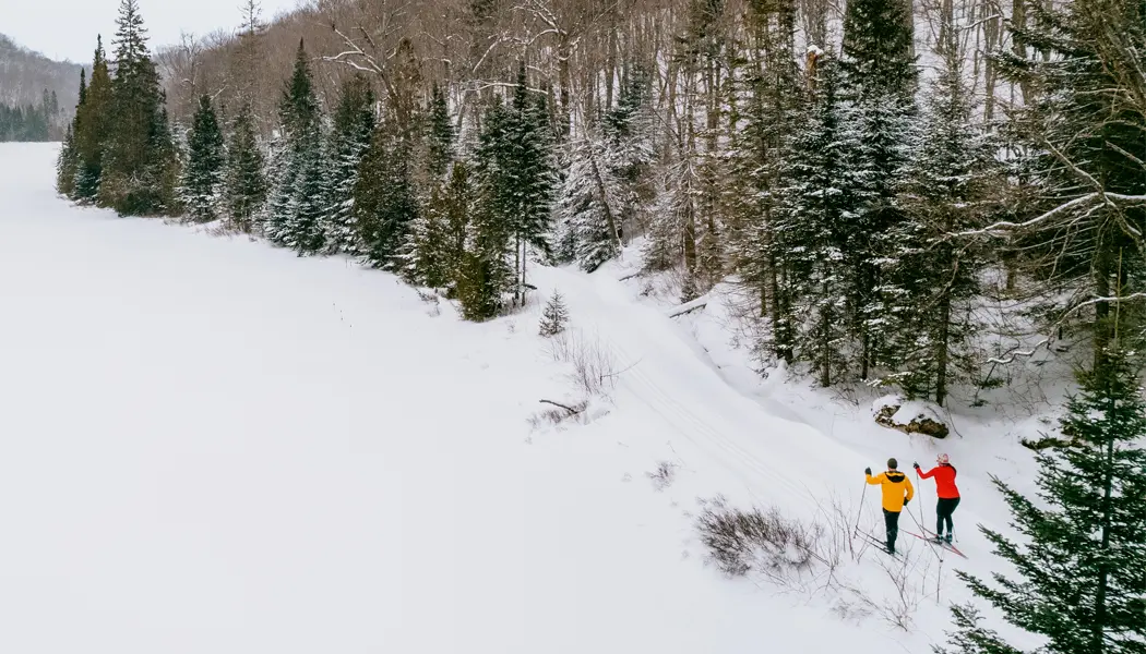 A couple cross-country skiing on a snowy trail alongside a forest at Stokely Creek Lodge.