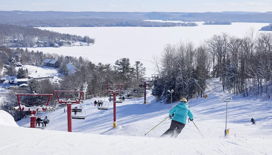 파란색 겨울 코트를 입은 알파인 스키어가 머스코카의 히든 밸리에 있는 스키장에서 스키를 타고 내려오고 있습니다.