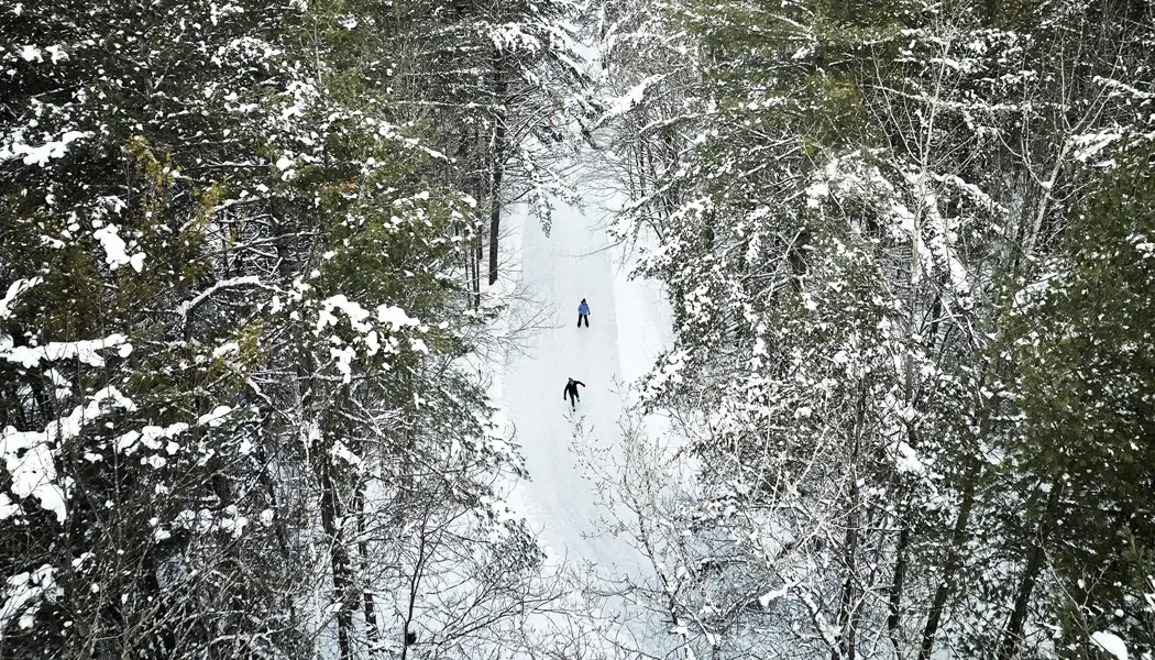 Vista aérea de dos personas patinando sobre hielo en una pista de patinaje bien mantenida a través del bosque en Arrowhead Park.