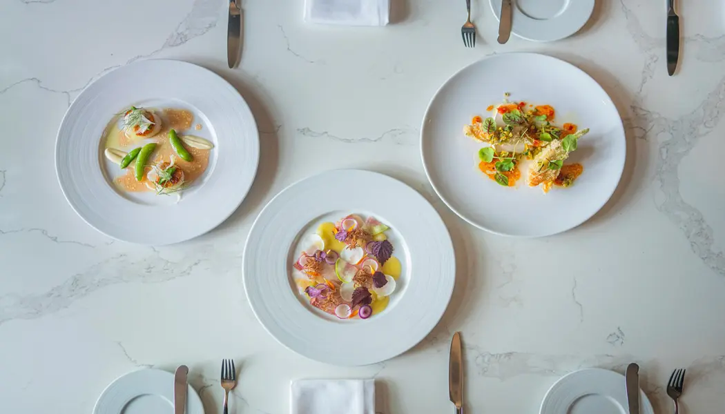 高級レストランで、白い食器とリネンのテーブルクロスの上に、食欲をそそる 3 品の食事が美しくセッティングされたテーブル。