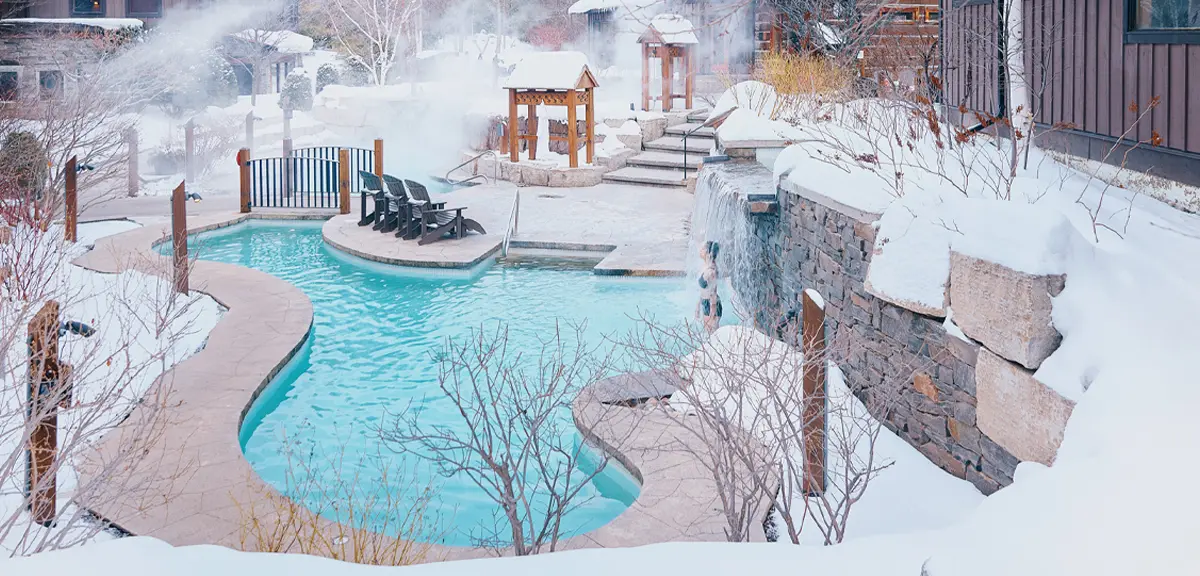 Über dem von Schnee umgebenen Außenwasserparcours des Scandinave Spa steigt Dampf auf.
