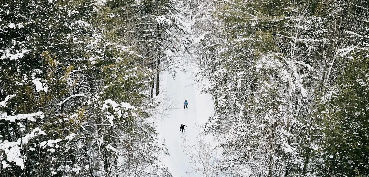Vue aérienne montrant deux personnes patinant sur un sentier de patinage bien entretenu dans la forêt du parc Arrowhead