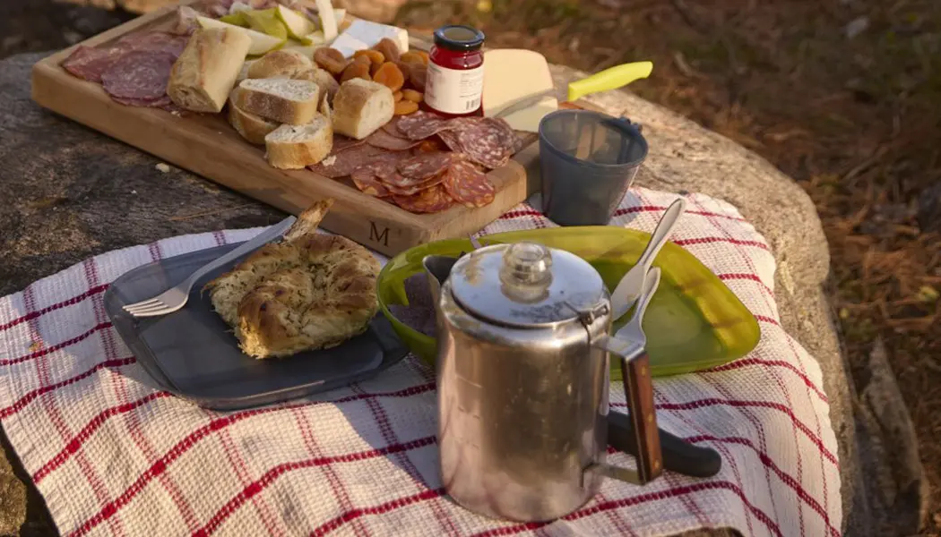 캠핑장에서 넓은 호수를 내려다보는 곳에서, 한 커플이 활활 타오르는 불 앞 통나무 벤치에 앉아 있습니다.