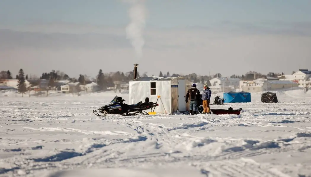 Ice anglers stand beside a snowmobile and an ice fishing hut on a frozen lake during the Wawa Ice Fishing Derby.