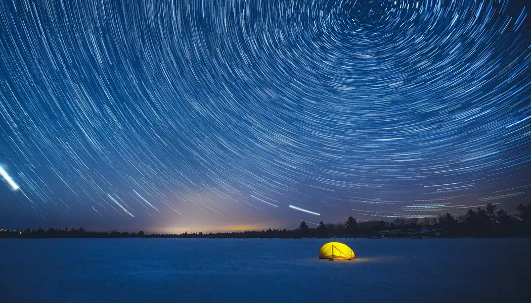 머스코카의 토런스 배런스에 있는 눈 덮인 밤 풍경 속의 노란색 텐트가 별이 빛나는 하늘의 밝은 빛 아래 밝게 빛나고 있습니다.
