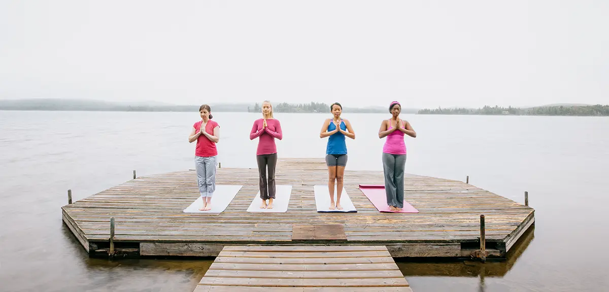 Group of people meditating on a wooden dock overlooking a calm lake.