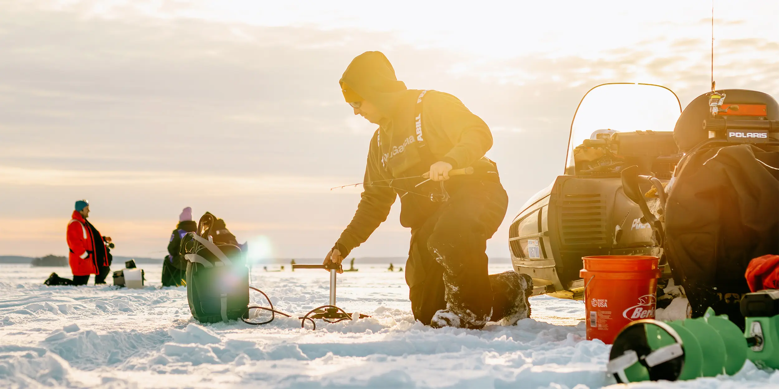 日の出の凍った湖で氷上釣り道具を準備する人々。