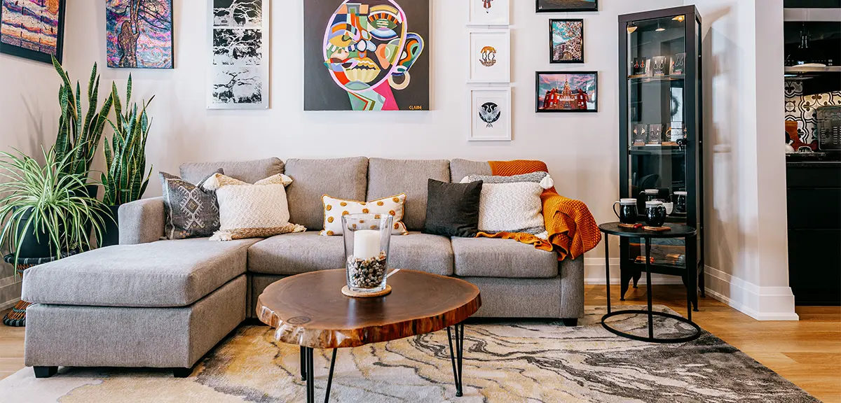 Salon moderne avec canapé d’angle, table basse et œuvres d’art colorées accrochées aux murs.