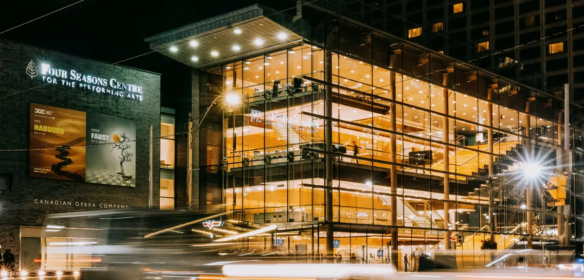 Glass-fronted performing arts building illuminated at night along a busy city street