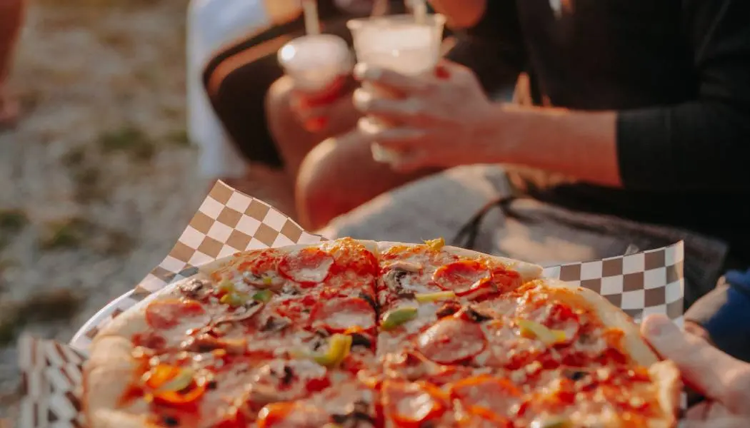 ビーチの近くで飲み物を手にした人々と焼きたてのピザ。