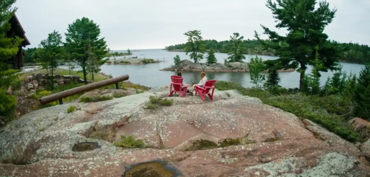 A man and a woman relaxing in deck chairs by a calm lake.