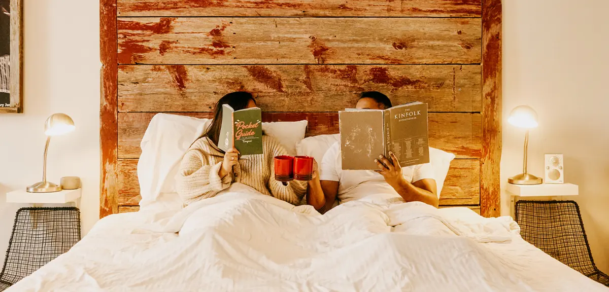 ベッドでマグカップを手に本を読んでいるカップル。