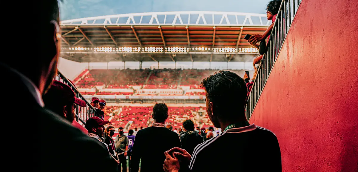 暗い曇り空がサッカー場の上に広がり、スタンドには人々が座っています。