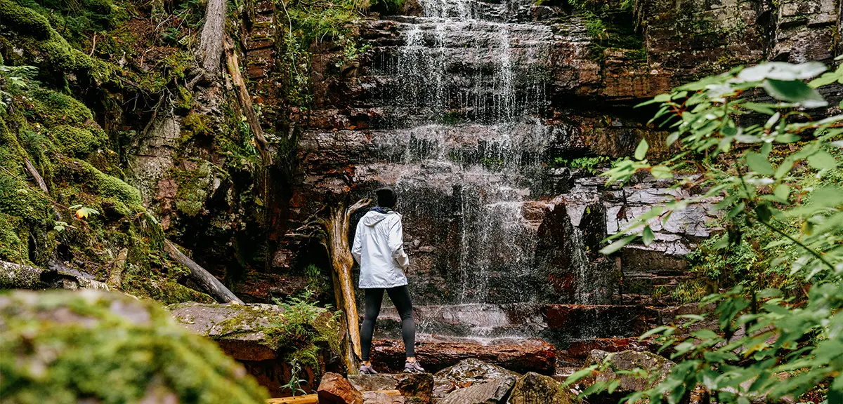 온타리오주 북부에서 한 등산객이 이끼 낀 바위, 나무, 울창한 녹음으로 둘러싸인 잔잔한 폭포를 감상하기 위해 잠시 멈춰 섰습니다.