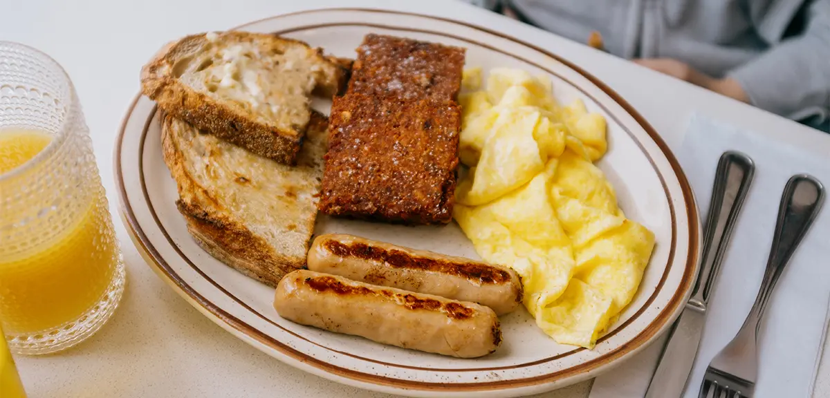 Plato de brunch con huevos revueltos, salchichas, tostadas y un vaso de zumo de naranja.