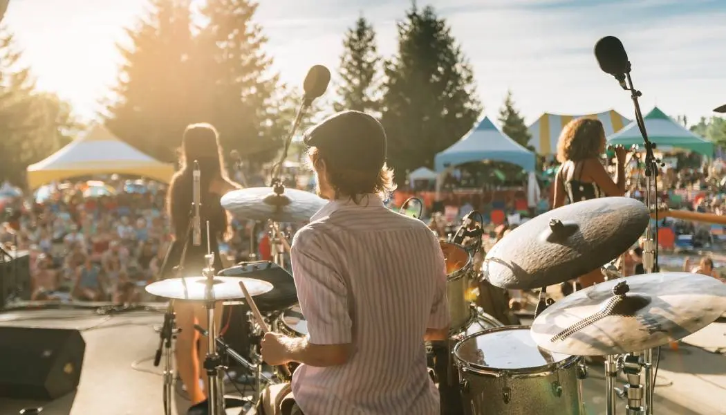 Ein Besucher des VELD Music Festivals sitzt mit ausgestreckten Armen auf den Schultern eines anderen, die hellen Scheinwerfer der Bühne beleuchten sie.