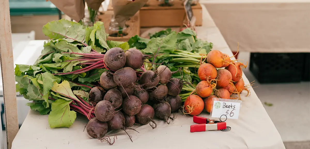  ファーマーズマーケットのテーブルに並べられた新鮮なビーツや野菜。背景には花が咲いている。