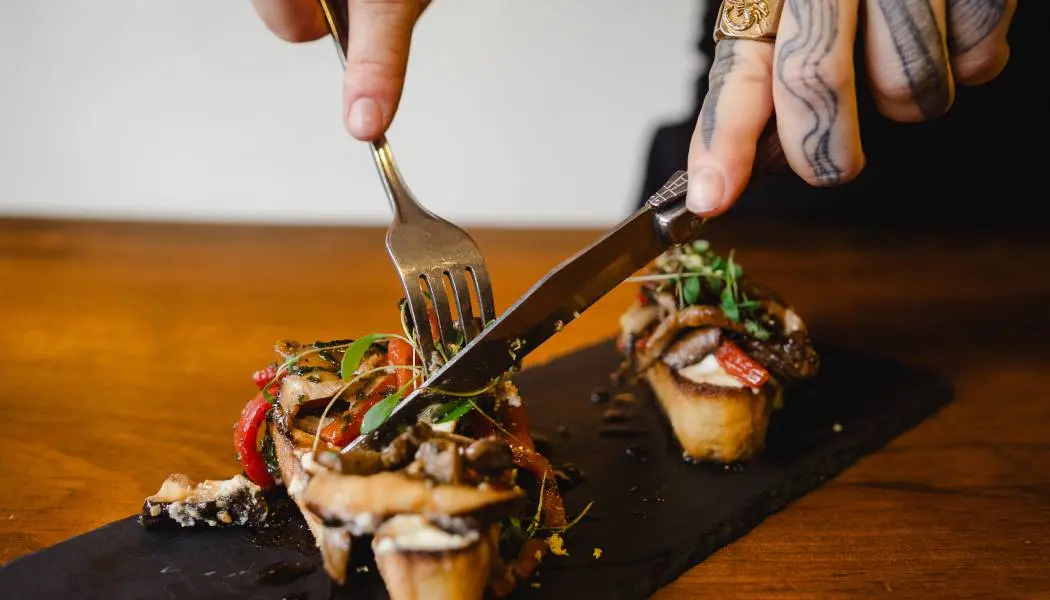 A person uses a fork and knife to cut into a stylishly plated appetizer dish at a Kingston restaurant.