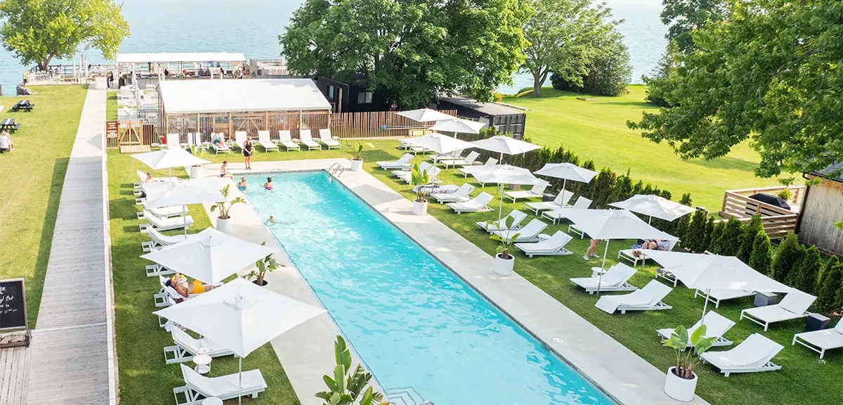 Outdoor pool with lounge chairs and umbrellas at Lakeside Motel in Prince Edward County overlooking the water.