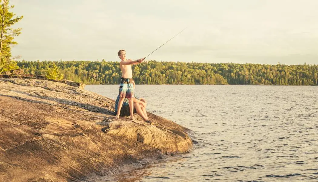 Un jeune garçon lance sa ligne de pêche depuis un rivage rocheux du parc provincial Quetico.