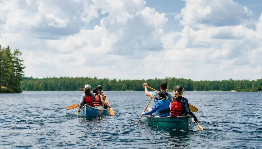 A group of six people paddles in two canoes across a calm lake in Kawartha Highlands Provincial Park.