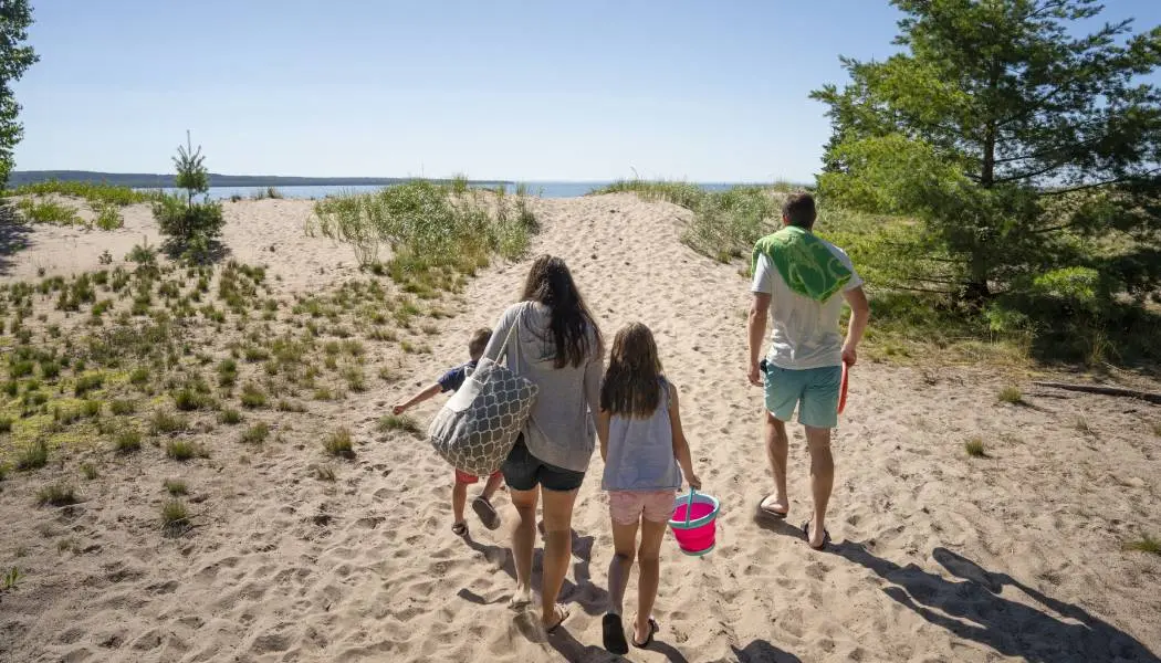 Eine vierköpfige Familie spaziert an einem warmen Sommertag auf einem sandigen Pfad entlang zu einem wunderschönen Strand am Lake Superior. 