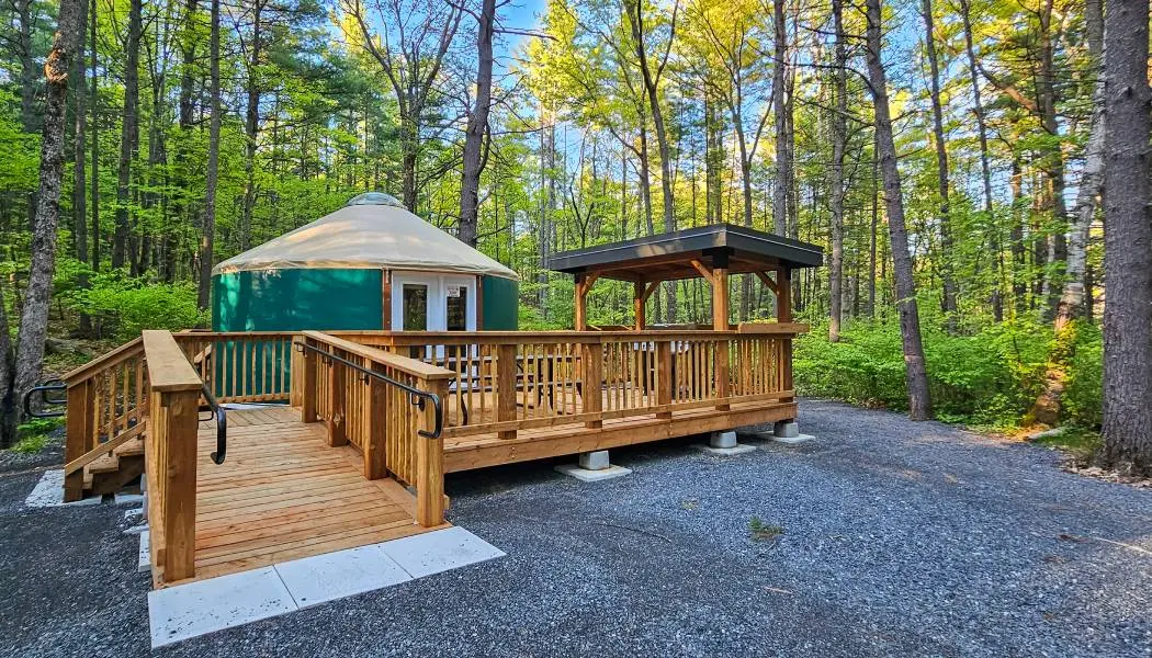 Un abri de camping en forme de yourte ronde, doté d'une rampe d'accès en bois, d'une terrasse extérieure et d'un coin salon.