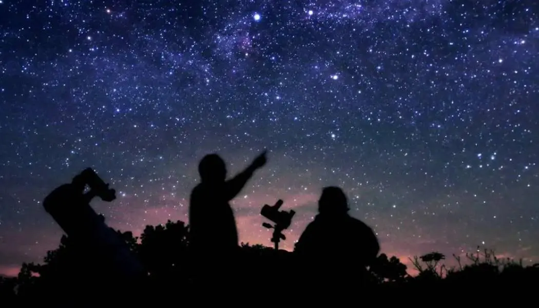 二人の人物が指をさして星空を見上げているシルエット。