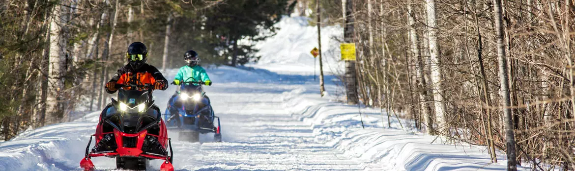 Two people riding snowmobiles on a well-maintained trail.