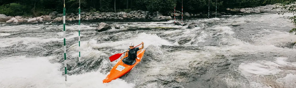  Un kayakista navega por rápidos de aguas bravas en un recorrido de slalom, pasando a través de postes de puerta numerados suspendidos sobre el río.