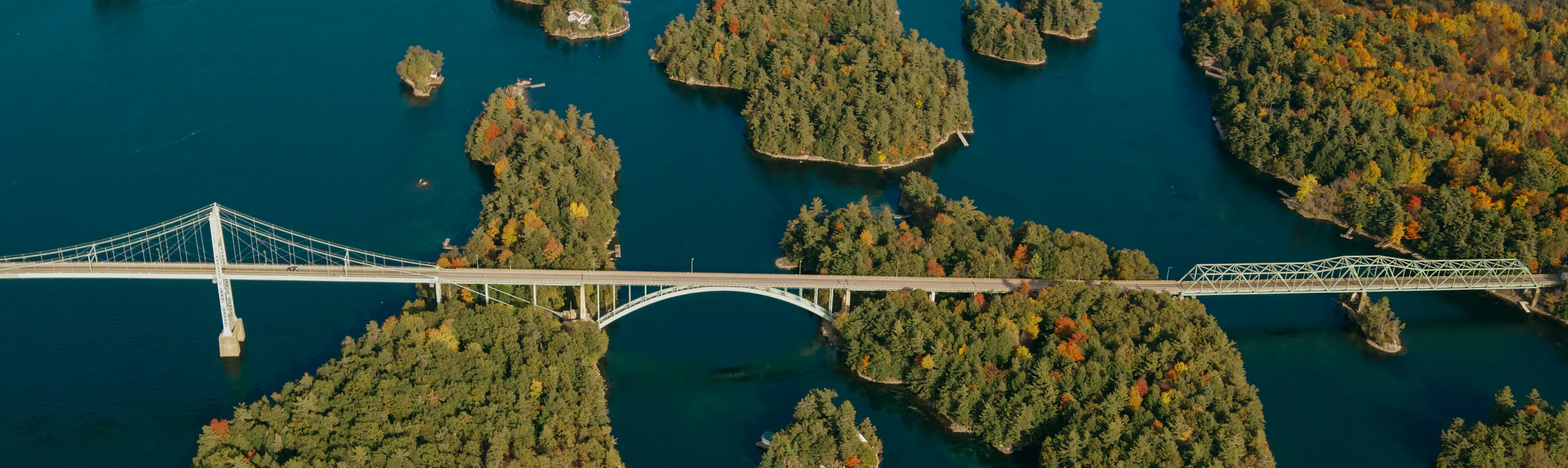南東オンタリオ州の秋の色彩に輝く、木々に覆われたサウザンド諸島を渡る橋の美しい空中写真。